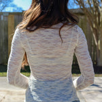 Person wearing a light-colored sheer sweater and jeans standing outdoors with trees and blue sky in the background