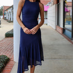 Woman in a navy blue dress standing on a sidewalk with buildings in the background