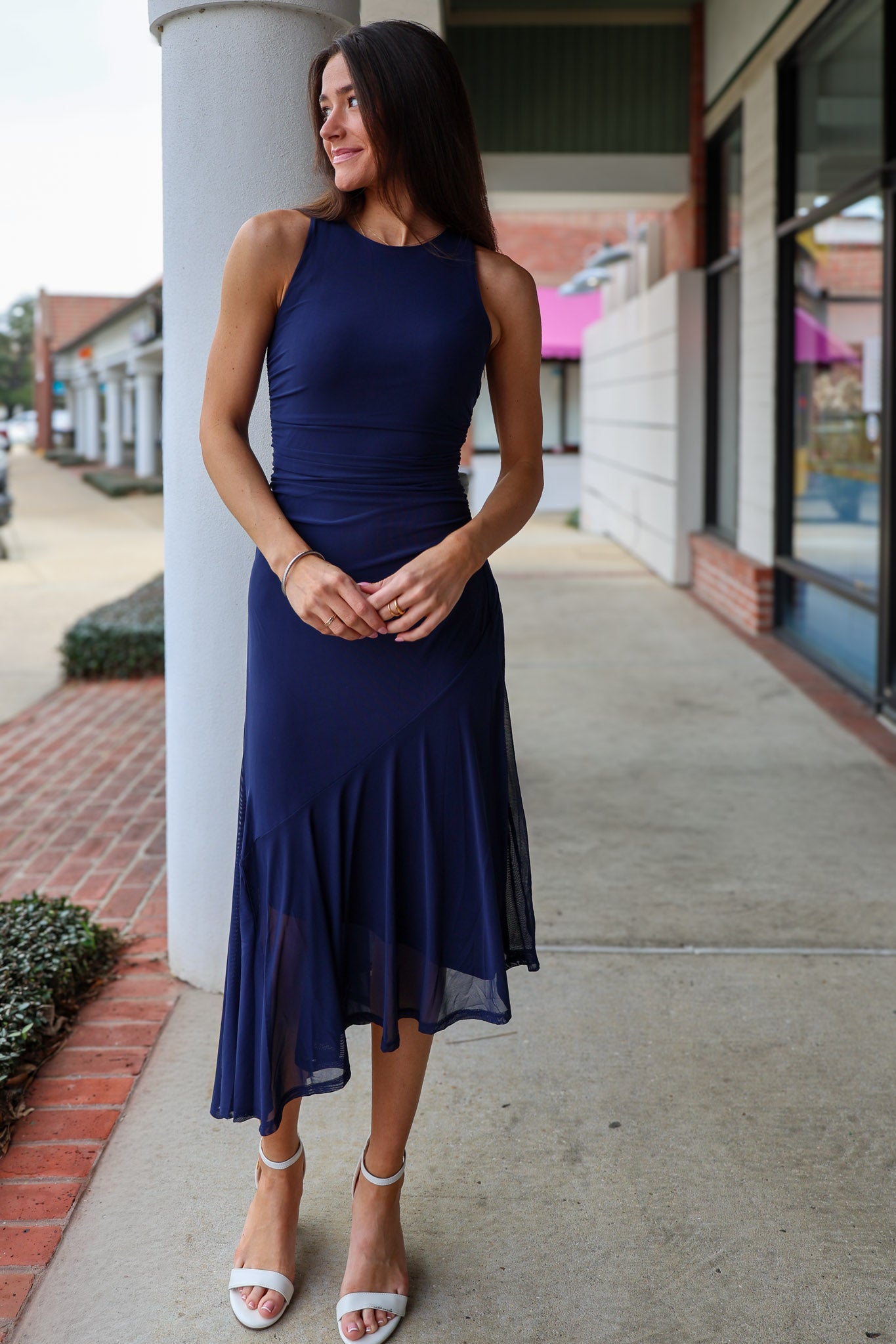 Woman in a navy blue dress standing on a sidewalk with buildings in the background