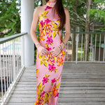 Woman in a floral dress standing on a wooden deck with greenery in the background