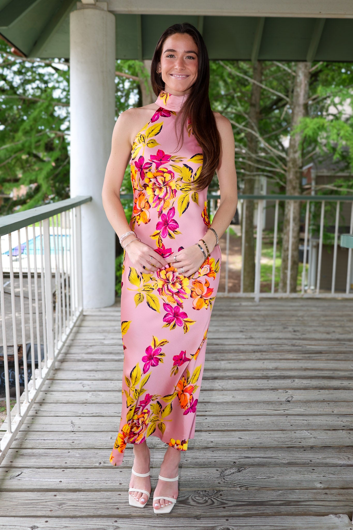 Woman in a floral dress standing on a wooden deck with greenery in the background
