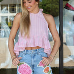 Woman wearing a pink striped top and denim shorts with floral patches.