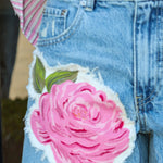 Denim shorts with a pink floral patch worn by a person.