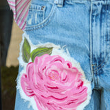 Denim shorts with a pink floral patch worn by a person.