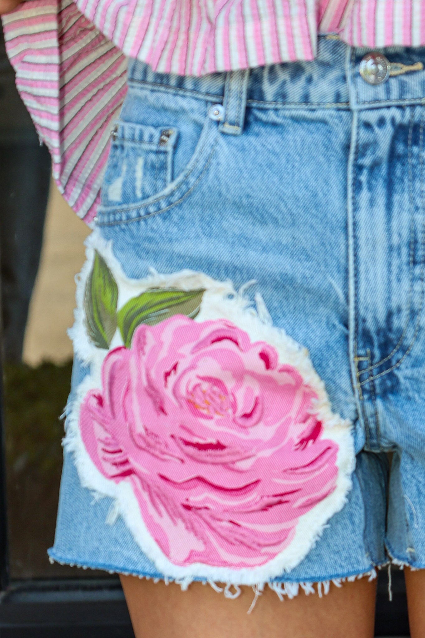 Denim shorts with a pink floral patch worn by a person.