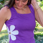 A woman wearing a purple sleeveless purple top with a large white flower applique on the front, paired with white bottoms, photographed outdoors at LSU.