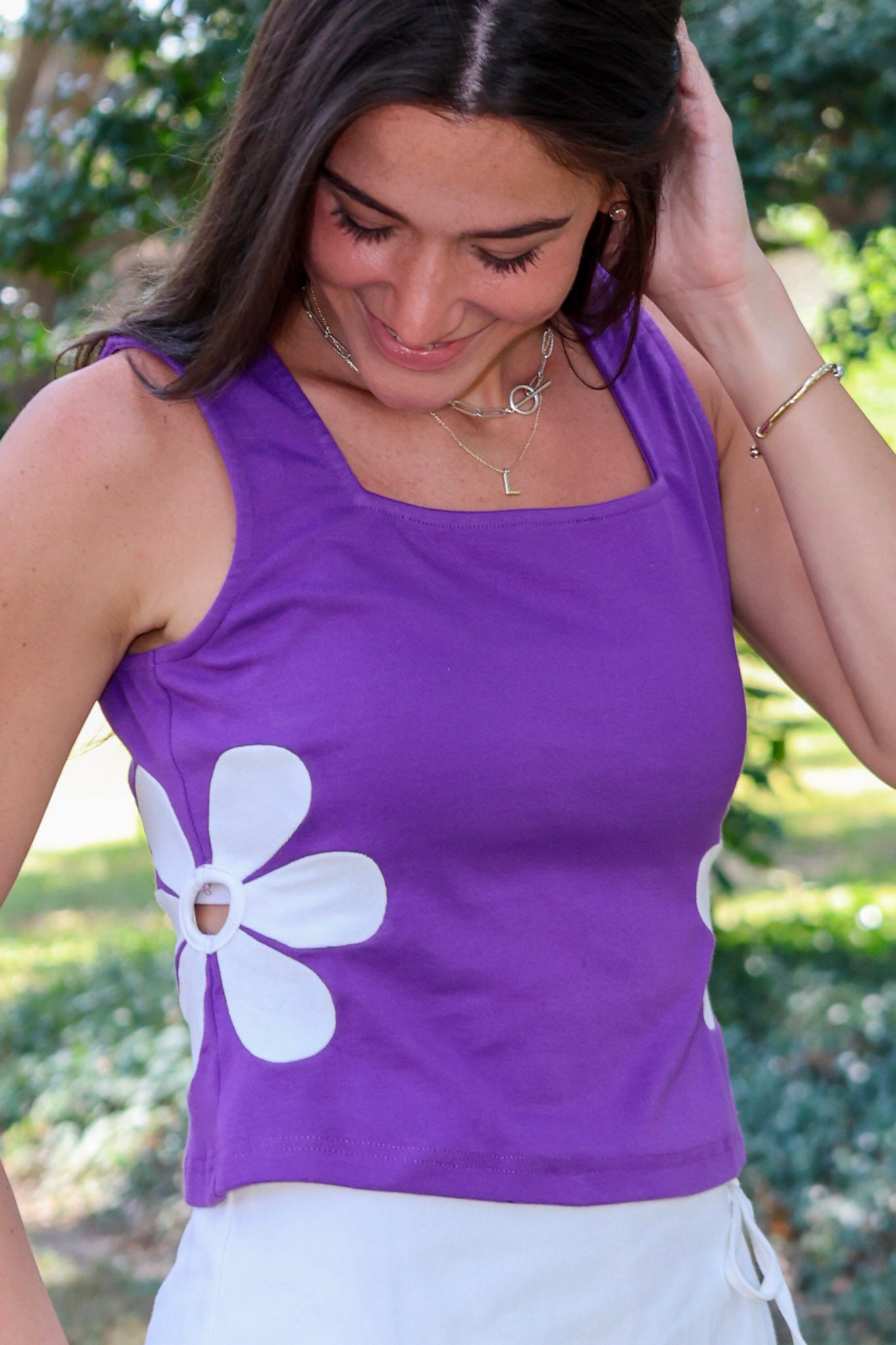 A woman wearing a purple sleeveless purple top with a large white flower applique on the front, paired with white bottoms, photographed outdoors at LSU.