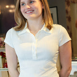 Woman wearing a white polo shirt and blue jeans indoors