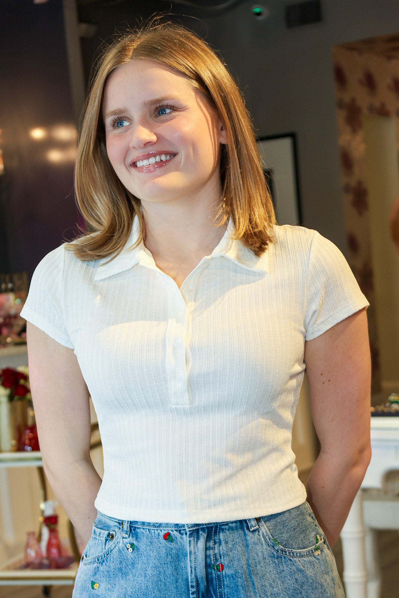 Woman wearing a white polo shirt and blue jeans indoors