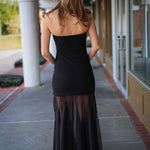 Woman in a strapless black dress walking on a sidewalk