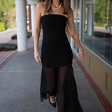 Woman wearing a strapless black dress with sheer overlay on a sidewalk.