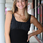 Woman wearing a black tank top and blue jeans standing outdoors.