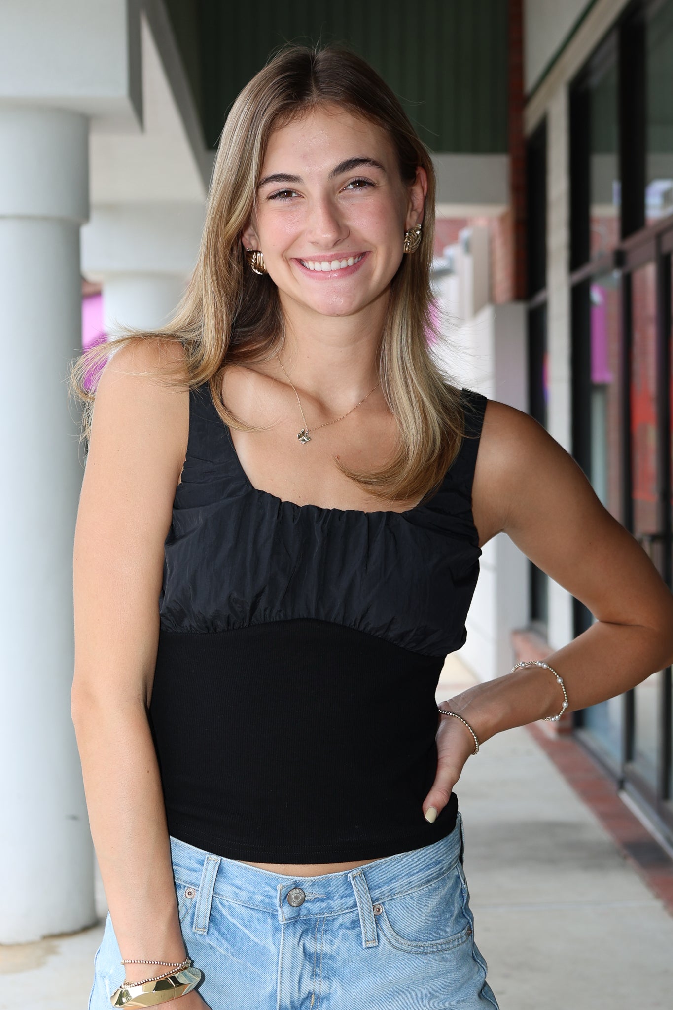 Woman wearing a black tank top and blue jeans standing outdoors.