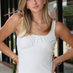 Woman wearing a white tank top and denim shorts standing outdoors.