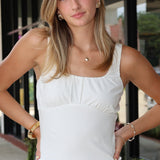 Woman wearing a white tank top and denim shorts standing outdoors.
