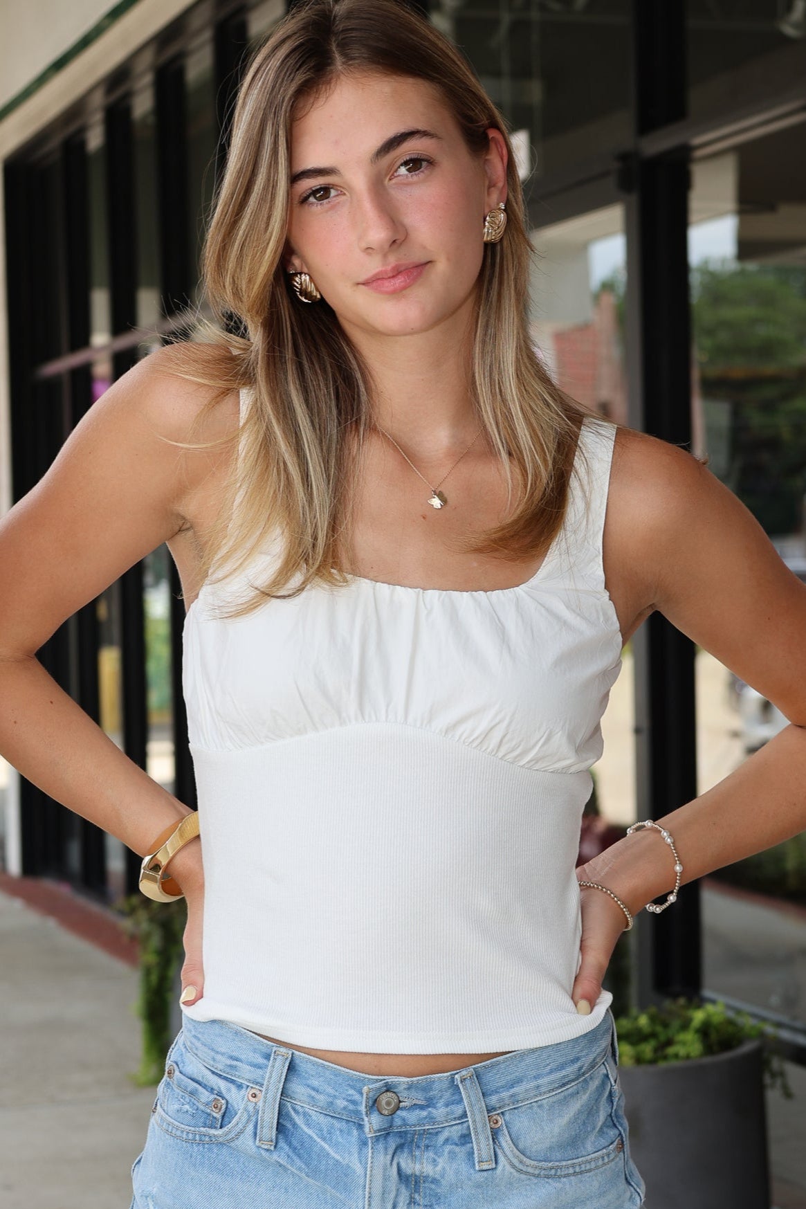 Woman wearing a white tank top and denim shorts standing outdoors.