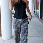 A woman walking outdoors wearing a black lace-trimmed camisole top and wide-leg pants with a blue, gray, and white tiger print.