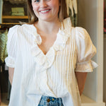 Woman wearing a white blouse with ruffled details and blue jeans in a store setting.