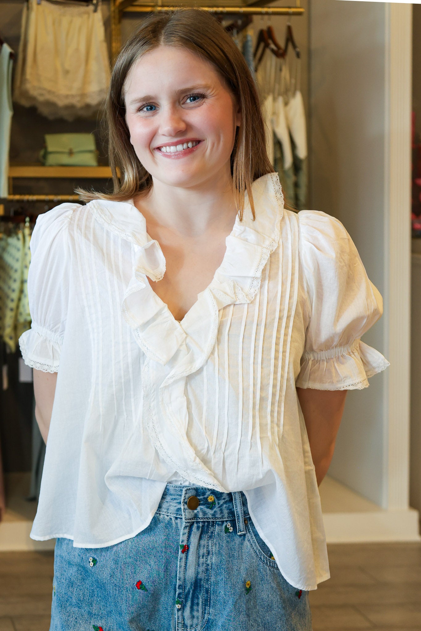Woman wearing a white blouse with ruffled details and blue jeans in a store setting.