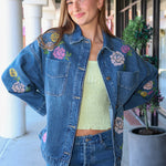 Woman wearing a denim jacket with floral embroidery in an outdoor setting