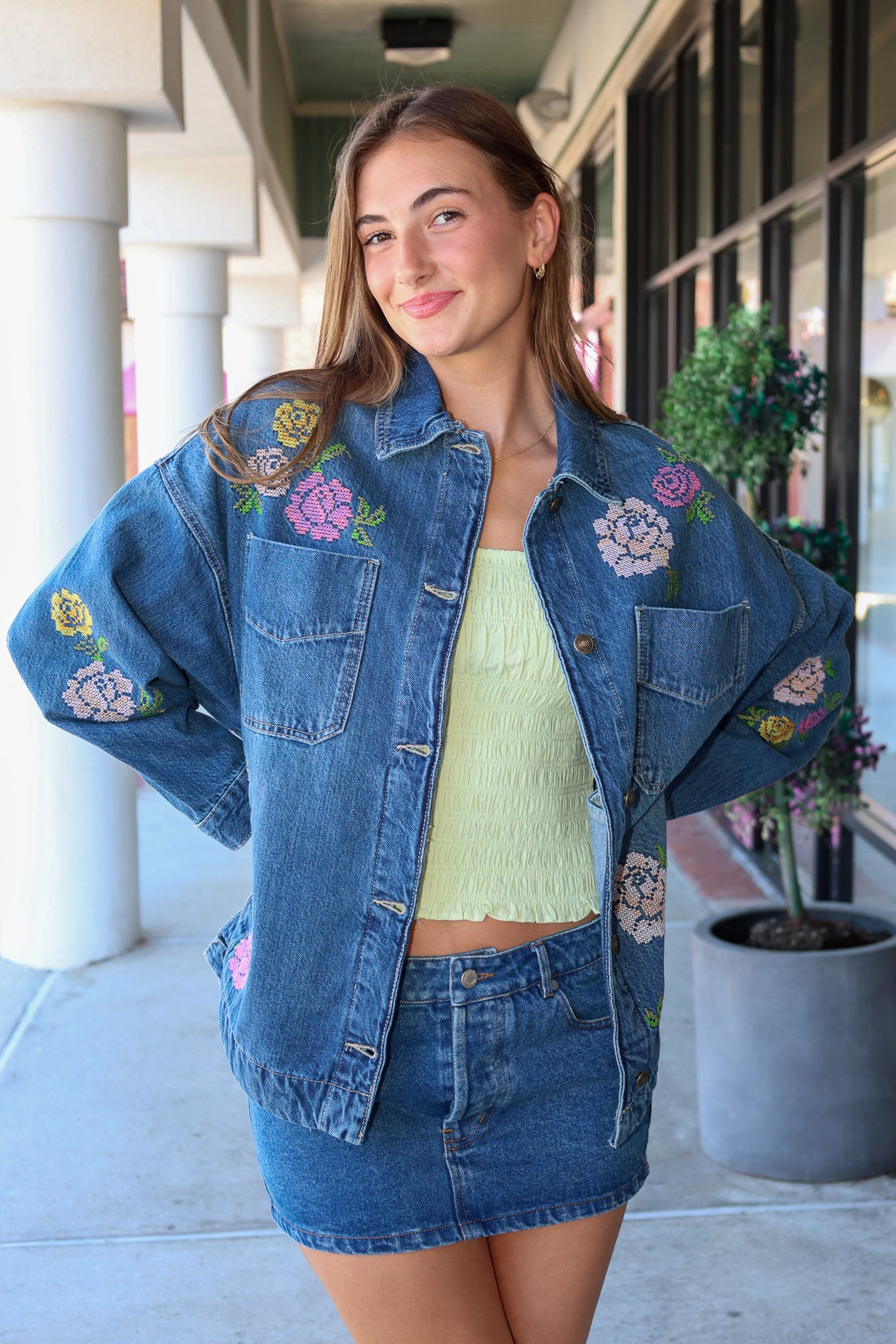 Woman wearing a denim jacket with floral embroidery in an outdoor setting