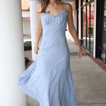 Woman in a light blue dress standing on a sidewalk.