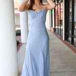 Woman wearing a blue plaid midi dress standing on a sidewalk.