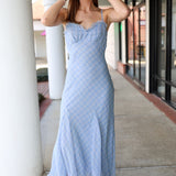 Woman wearing a blue plaid midi dress standing on a sidewalk.