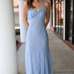 Woman wearing a light blue patterned dress standing on a sidewalk.