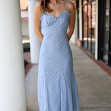 Woman wearing a light blue patterned dress standing on a sidewalk.