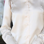 A close-up of a woman wearing a long-sleeve white satin button-up shirt with blue jeans.