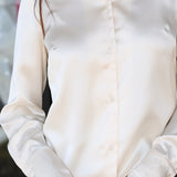 A close-up of a woman wearing a long-sleeve white satin button-up shirt with blue jeans.