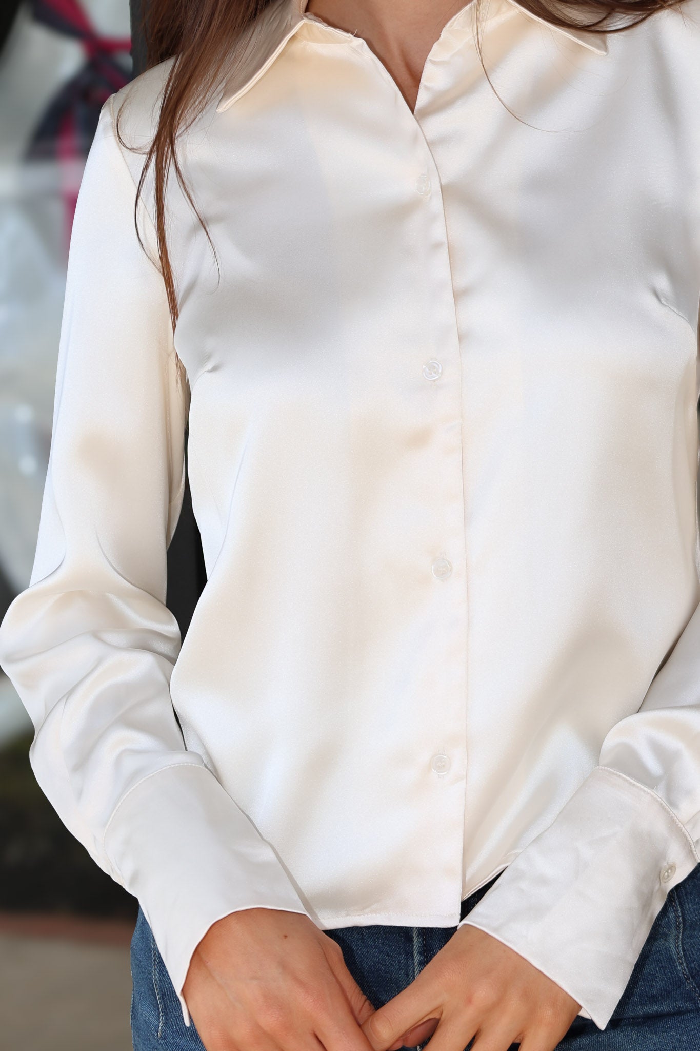 A close-up of a woman wearing a long-sleeve white satin button-up shirt with blue jeans.