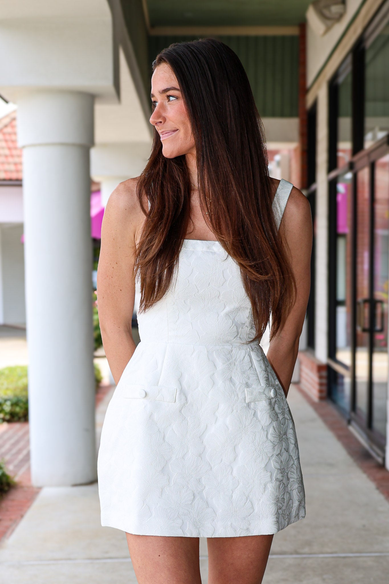 Woman in a white jaquard romper dress standing outdoors on a sidewalk.