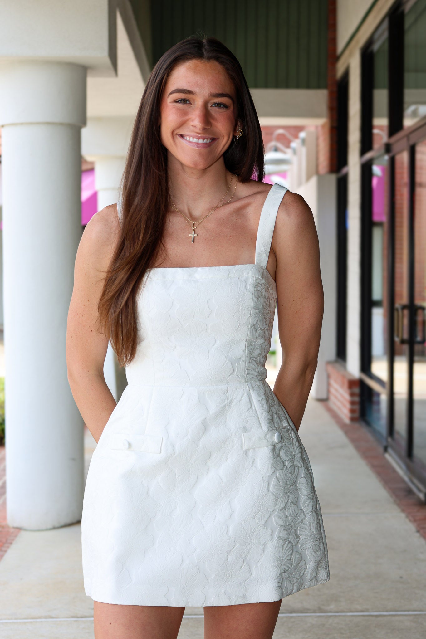 Woman in a white jaquard floral dress standing outdoors near a building