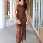 Woman in a brown dress holding a clutch on a sidewalk