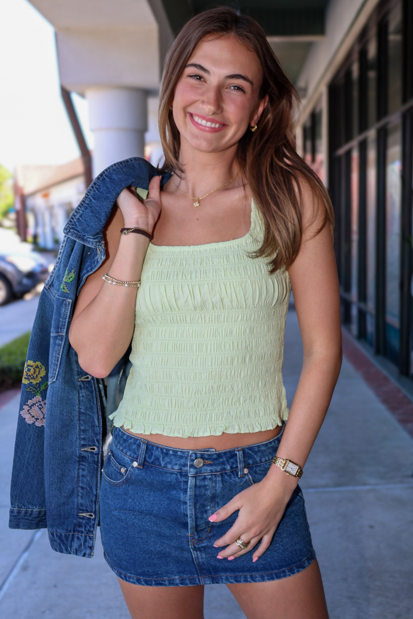 Woman wearing a light green top and blue denim skirt, holding a denim jacket.