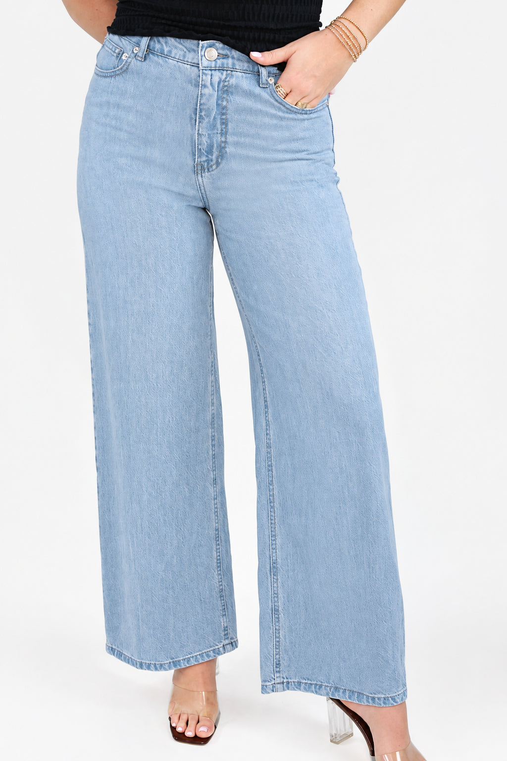 A person wearing Z Supply light-wash wide-leg denim jeans with a black top and white sneakers, standing against a plain white studio background.