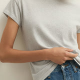 Woman wearing a gray t-shirt and blue jeans against a white wall