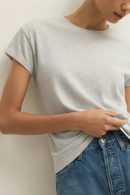 Woman wearing a gray t-shirt and blue jeans against a white wall