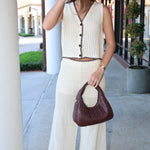 Woman in a ivory crochet outfit holding a brown handbag on a sidewalk.