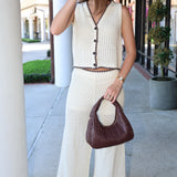 Woman in a ivory crochet outfit holding a brown handbag on a sidewalk.