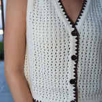 White crochet top with brown trim worn by a person, blurred background
