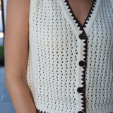 White crochet top with brown trim worn by a person, blurred background