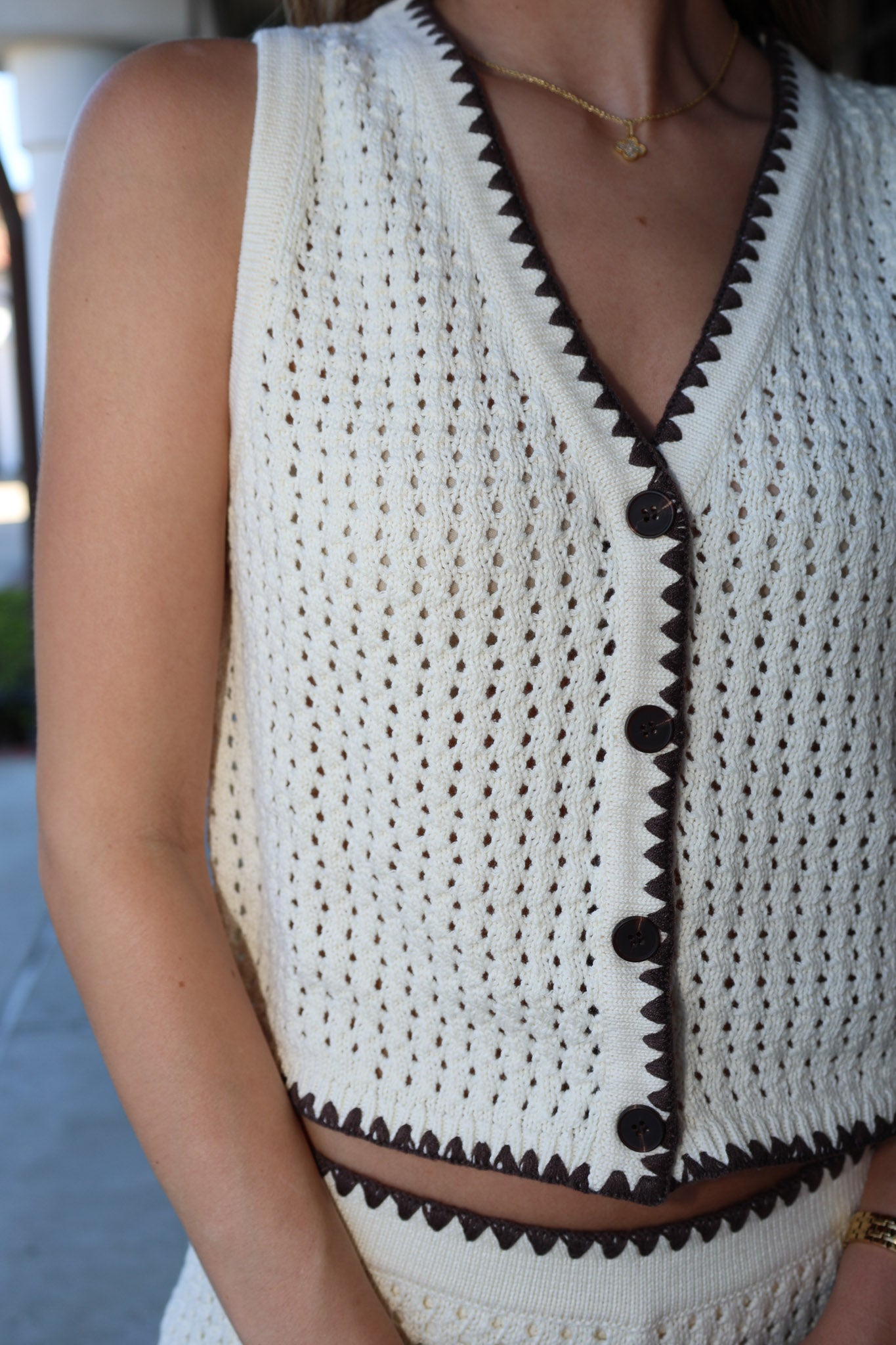 White crochet top with brown trim worn by a person, blurred background