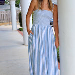 Woman wearing a blue and white striped dress standing outdoors near columns.