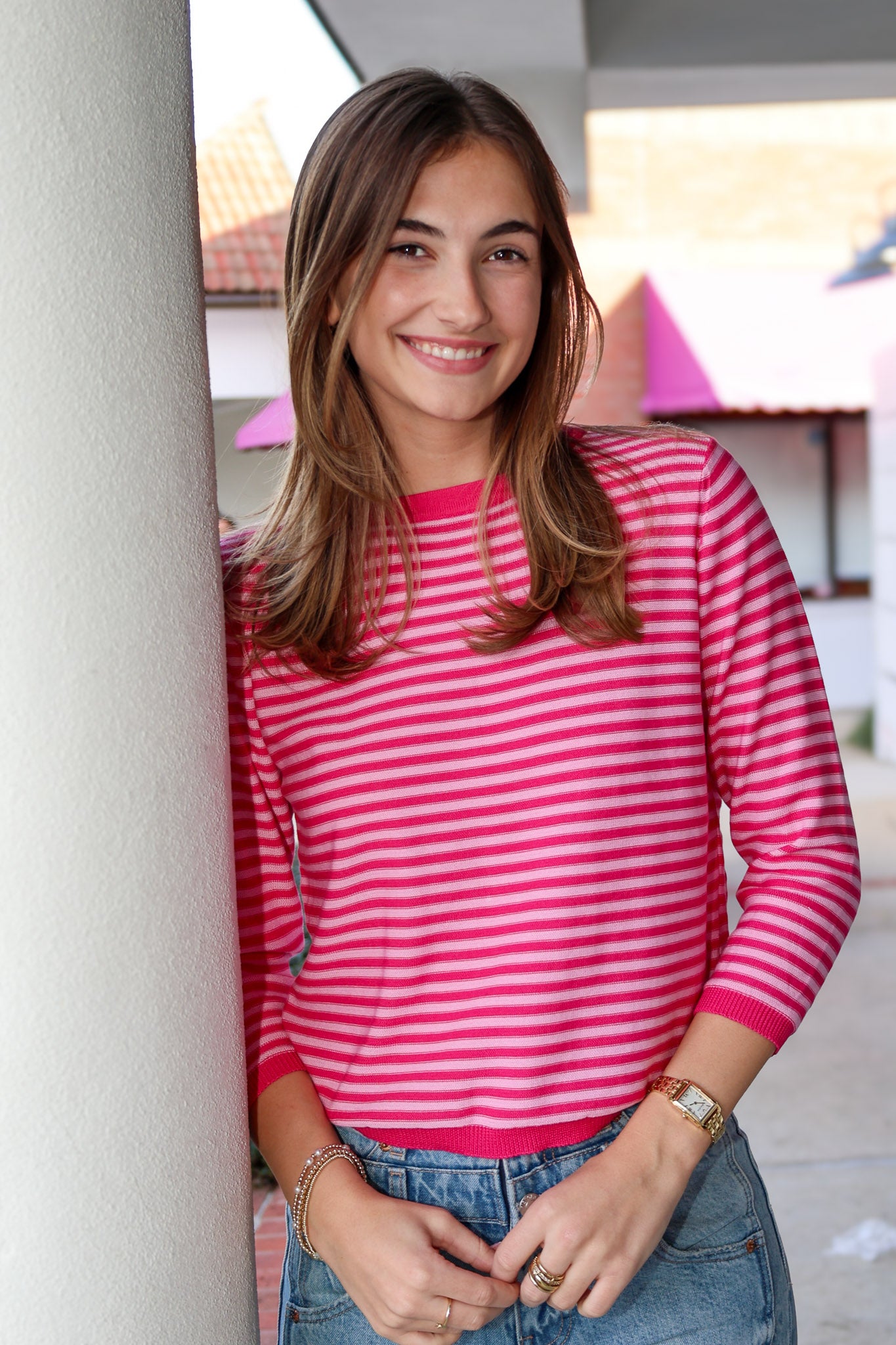 Woman wearing a pink striped shirt standing against a building.