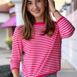 Woman wearing a pink striped sweater and blue jeans, standing outdoors.