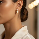 A close-up side profile of a woman wearing a delicate gold and pearl drop huggie earring,