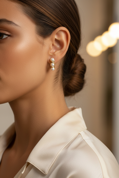 A close-up side profile of a woman wearing a delicate gold and pearl drop huggie earring,